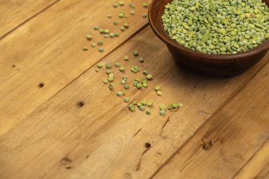 Kuru bezelye. Kahverengi kil kase. Ahşap bir arka plana yeşil bezelye serpilmesi. Pişmemiş yemek. Sağlıklı yiyecekler. Yakın plan. Seçici odaklanma. Metin ve tasarım ögeleri için boşluk kopyala.