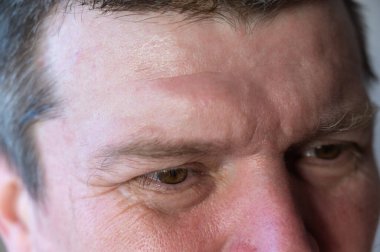 - Erkek yüzünün üst kısmı. Gözlerinde kırışıklıklar olan olgun bir adam. Kahverengi kısa saç. Yakın plan. Seçici odak.