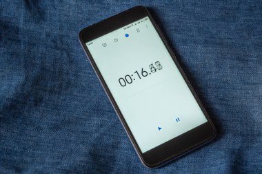 Aygıtın ekranında çalışma süresi. Stopwatch uygulaması açık olan siyah akıllı telefon. Bitmek bilmeyen zaman kavramı. Kot pantolona karşı..