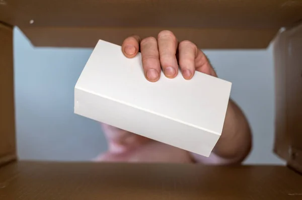 一个男人从一个纸板箱里掏出一个白色的长方形盒子 白色包装中的智能手机或其他电子设备 底部的观点 有选择的重点 — 图库照片