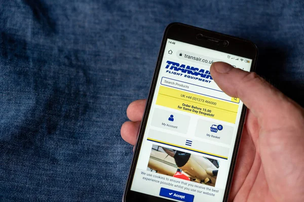Transair Ana Sayfası. Uçuş Malzemeleri ve Pilot Atölyesi, genel havacılık pilotları ve uçuş eğitim merkezleri için malzeme ve pilot malzemeleri sağlıyor. Erkek eli telefonu tutuyor. Ukrayna, Mykolaiv - 06 29 2022