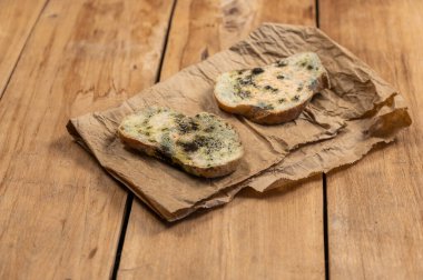 Ahşap arka planda küflü ekmek. Mantar kalıbıyla kaplı iki dilim buğday ekmeği. Ekmek kahverengi bir kese kağıdının üzerinde yatıyor. Bozuk yemek. Seçici odak.