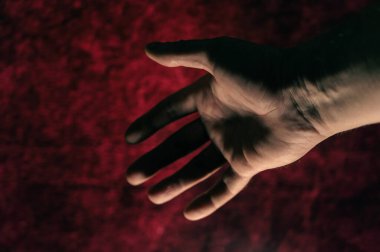 Koyu kırmızı arka planda yetişkin bir adamın açık avucu. Selamlama, tokalaşma hareketi. Yakın plan. Seçici odaklanma. Odaklanma, gürültü, tahıl etkisi.