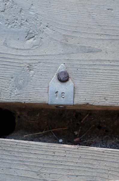 An old dirty floorboard with an aluminum tag on it. The tag has the number 18 stamped on it. Cracked boards with gaps between them. Top view. Selective focus.