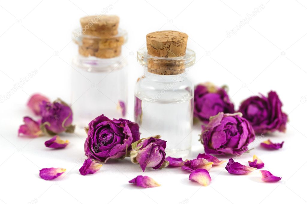 Two fragrance bottles filled with rose aroma oil with purple dried rose buds and petals isolated on white background.