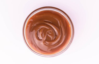 Bowl of sweet caramel sauce on a white plate, top view. clipart