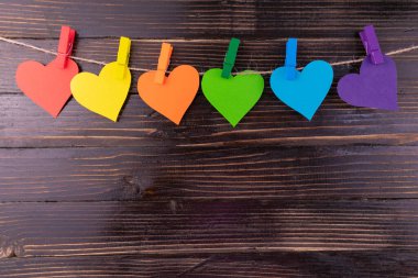 Gökkuşağı renginde kalpler, siyah ahşap arka plandaki mandallara asılır. LGBT sembolü. Boşluğu kopyala.