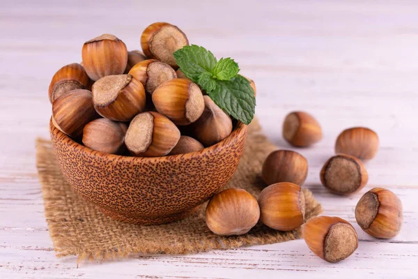 Beyaz ahşap bir arka planda tahta bir kasede kabuklu fındıklar. Yakın plan..