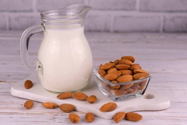 Beyaz arka planda şeffaf bir sürahide badem sütü.
