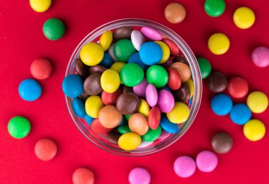  Parlak kırmızı arka planda bir kasede çok renkli şekerler. Üst manzara.