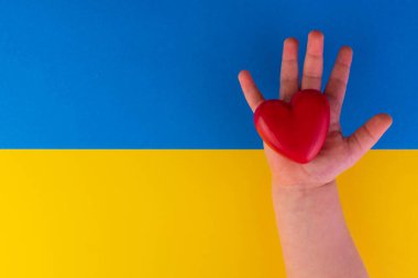 Ukrayna bayrağının arka planında bir çocuğun elinde kırmızı kalp. Ukrayna 'daki savaşa karşı kavram..