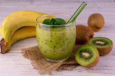 Vitamin smoothie from kiwi and banana on a white wooden background.