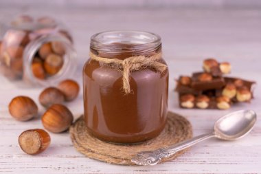 Beyaz ahşap arka planda fındıklı çikolata kaplı kavanoz..