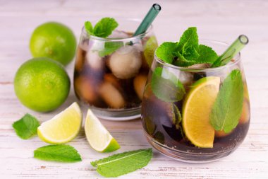  Küba Libre kokteyli. Beyaz ahşap arka planda taze limon, kahverengi rom ve buz küpleri..