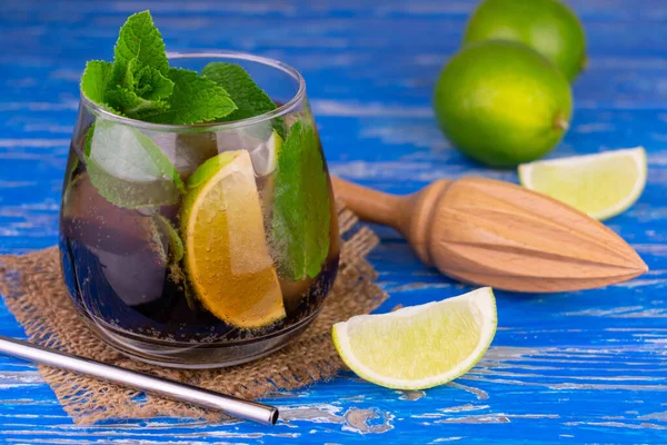 Cocktail Cuba Libre with lime, rum, mint and ice on an old blue wooden background.