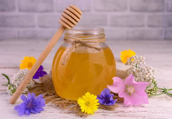 Flower honey in a jar and fresh wildflowers.