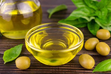 Cam bir kasede zeytinyağı ve koyu arkaplanda balelik yaprakları.