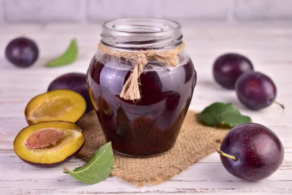 stock image Homemade plum jam in a glass jar on a white wooden background.