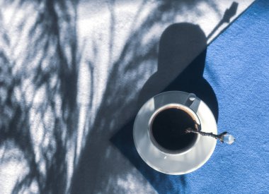 Beyaz fincanda kahve, mavi ve beyaz arka planda kaşık, düz bir zeminde, botanik gölgeleri kuru yabani otlar gibi uzanıyordu.