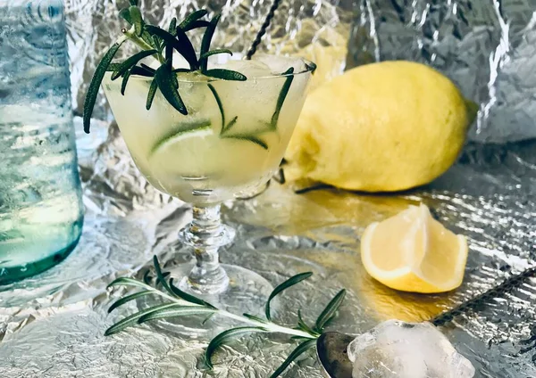 Cold lemon drink into which one can add some alcohol with ice cubes and mint on steel background with candles
