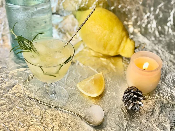 Cold lemon drink into which one can add some alcohol with ice cubes and mint on steel background with candles