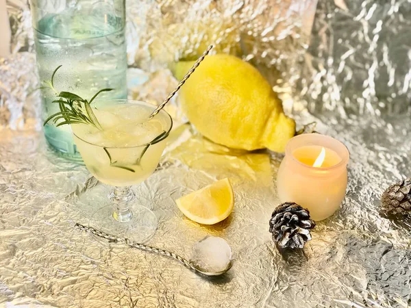 Cold lemon drink into which one can add some alcohol with ice cubes and mint on steel background with candles