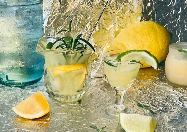 Cold lemon drink into which one can add some alcohol with ice cubes and mint on steel background with candles