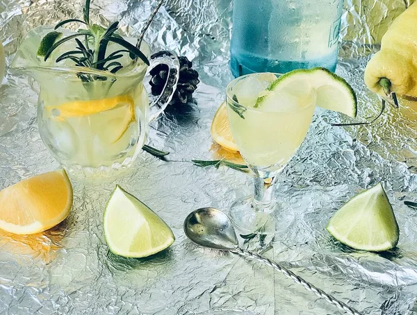 Cold lemon drink into which one can add some alcohol with ice cubes and mint on steel background with candles