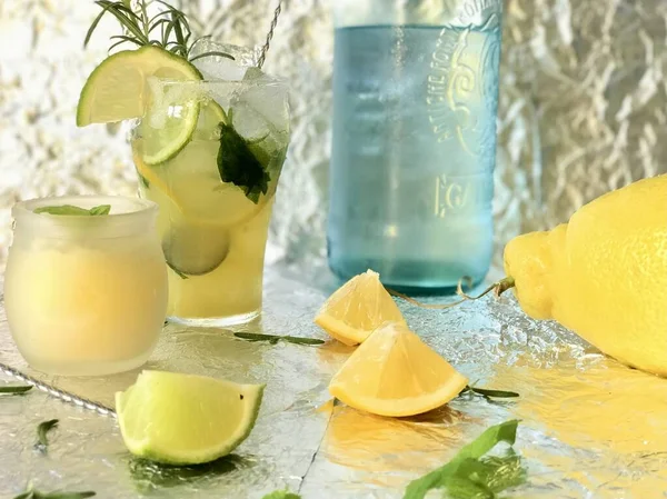 Cold lemon drink into which one can add some alcohol with ice cubes and mint on steel background with candles