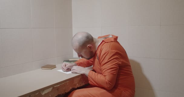 Prisionero en una celda de la prisión escribe una carta a lápiz y tira la hoja — Vídeos de Stock