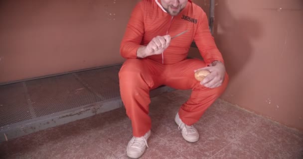 Prisoner in an orange uniform takes a rasp out of bread and rejoices. — Stock Video