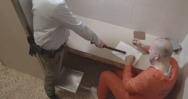 Elinde kauçuk copu olan gardiyan mahkûma itiraf yazdırıyor.