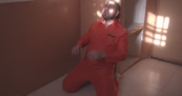 Smutný vězeň v oranžové uniformě klečí a dívá se z okna. — Stock video