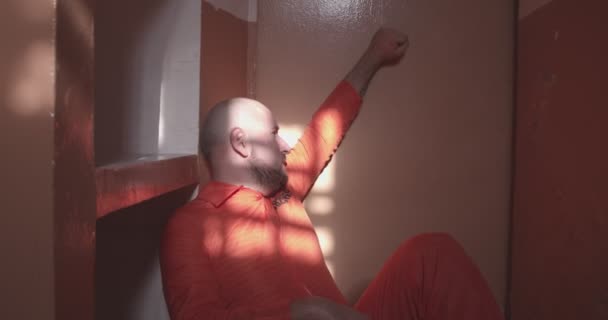 Плачущий заключенный сидит на полу и ударяется рукой о дверь тюремной камеры — стоковое видео