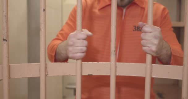 Les mains du prisonnier en uniforme orange tiennent les barreaux de la cellule de la prison. gros plan. — Video
