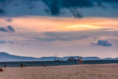 Tanınmayan plaj ziyaretçileri Pattaya Tayland 'daki Jomtien Sahili' nde eğlenirken gemiler okyanusta yüzüyor..
