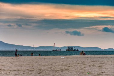 Tanınmayan plaj ziyaretçileri Pattaya Tayland 'daki Jomtien Sahili' nde eğlenirken gemiler okyanusta yüzüyor..