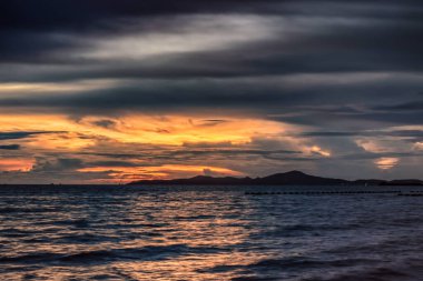 Pattaya Tayland 'daki Jomtien Sahili' nin derin ve canlı bir günbatımı. Uzak sahil bir siluet gibi görünür ve bulutlar karanlık okyanusun üzerinde dramatiktir..