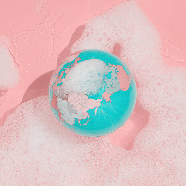 2022. Globe floats in a lather against pastel pink background. Minimal environmental abstract scene. Concept of caring for the planet and cleaning the planet. Ecological card idea. 