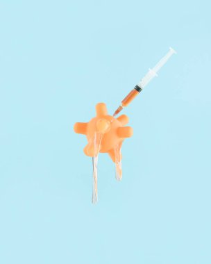 Balçık, şırınga ve iğneyle koronavirüs modeli, izole edilmiş mavi arka planda erir ve çürür. Aşıdan sonra soyut sürrealite yaratıcı konsept. Minimum kart. Covid-19 salgınını sonlandır.