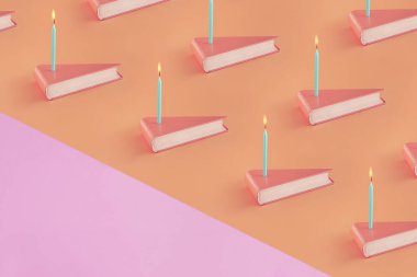 Üçgen şekilli kitaplar, izole edilmiş pastel mercan turuncu arka plan ve pembe fotokopi alanı üzerine doğum günü mumları. Asgari soyut yaratıcı model. Okul kutlaması ya da yıldönümü kavramı. Not kartı..