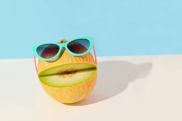 Happy emoji with sunglasses and smile made of melon on isolated vivid blue and pastel beige background. Abstract creative summer fruit scene. Ocean beach party. Vacation concept. Sun and shadow.
