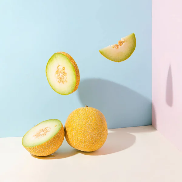 Minimal abstract creative summer fruit scene made of melon and juicy melon slices flying in the space on isolated pastel beige, blue and pink background. Sun and shadows. Raw dessert food or vacation idea.