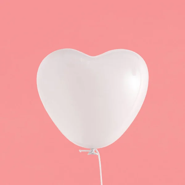 White heart-shaped balloon floats in space on isolated pastel coral-pink background with copy space. Minimal abstract valentines party concept. Invitation, greeting or gift card. Love symbol.