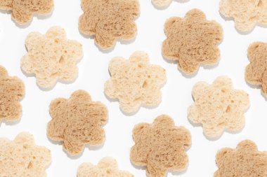 Creative abstract pattern made of flower shaped cut-outs from slices of white and whole-grain brown toast bread on isolated pastel white background. Minimal flat lay texture. Food comparison or health benefits concept.