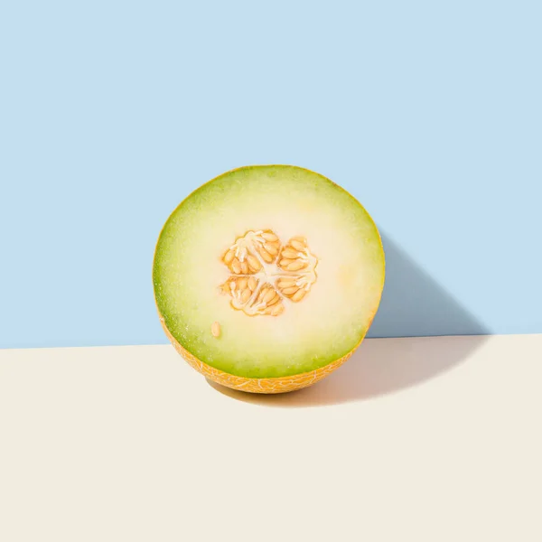 Halved sunlit melon standing on isolated pastel beige background leaning against the blue wall. Sun and shadow. Minimal abstract creative agriculture idea. Raw food or summer fruit concept.