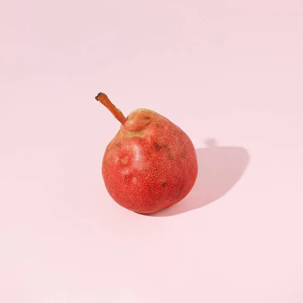 Red, ripe, juicy sunlit pear against pastel pink background. Sun and shadow. Minimal abstract natural idea of organic food, healthy eating or farming. Minimal autumn fruit scene. Agricultural concept.