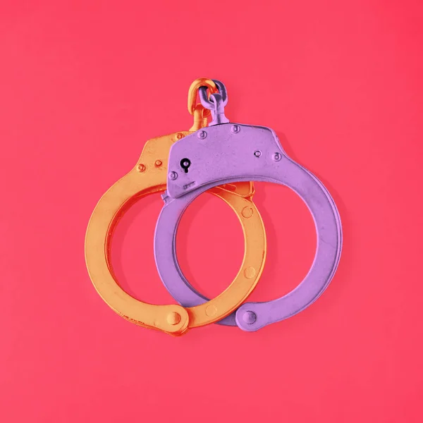 Locked golden purple handcuffs on isolated vibrant pink background. Minimal concept of relationship, marriage, engagement or closely associated couple. Unbreakable or eternal love. Valentine\'s symbol.
