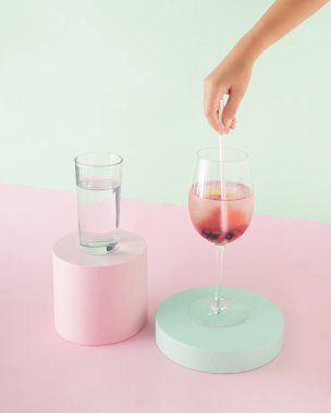 Childs 'ın eli kağıt kamışları taze kırmızı böğürtlenli detoks suyuna koyuyor. İzole edilmiş pastel pembe ve yeşil arka plan. Yaz partisi sağlıklı içeceklerinin minimum konsepti. Yaratıcı kart.