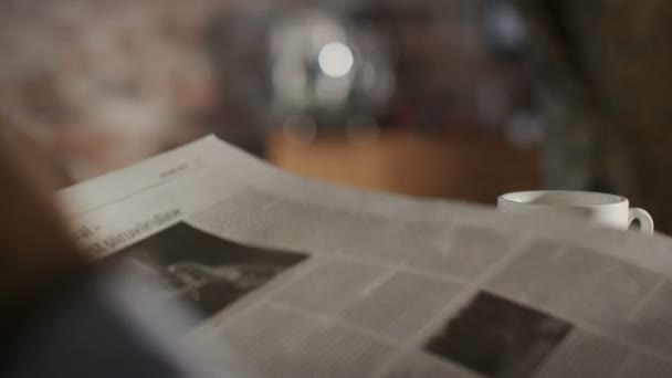 Человек читает газету и пьет кофе дома — стоковое видео